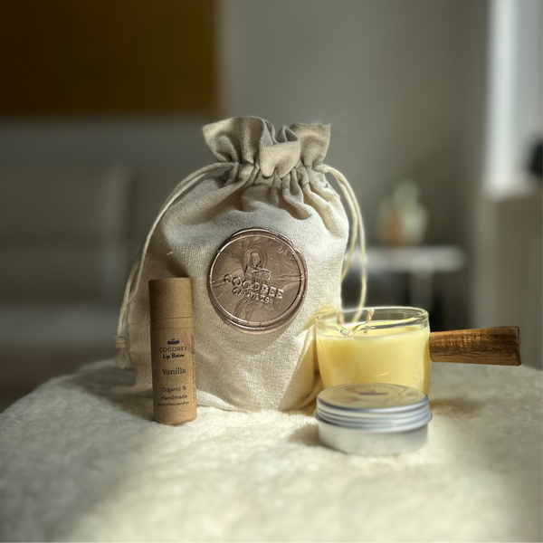 A set of skincare products including a moisturizing candle, balm, and lip balm, displayed alongside a reusable linen pouch with a product label visible.
