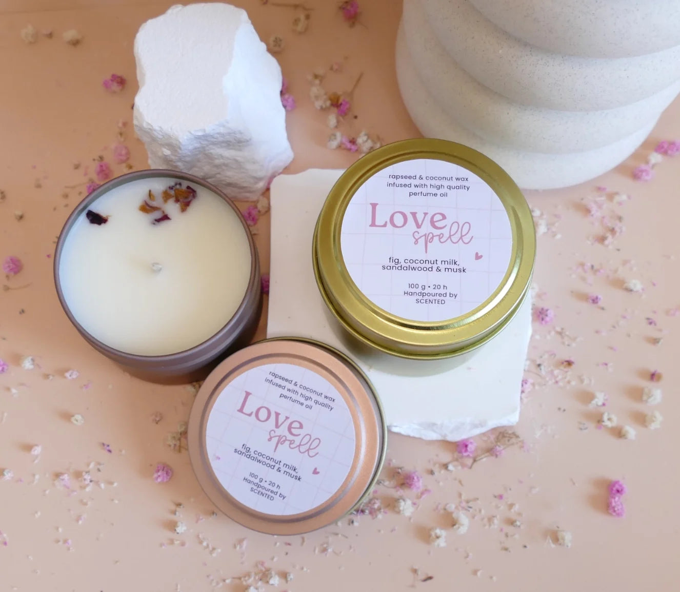 Manjša naravna dišeča sveča Love Spell v roza ali zlati embalaži – zapeljiva lesno-cvetoča aroma s pudrastimi notami, popolna za čutne večere.