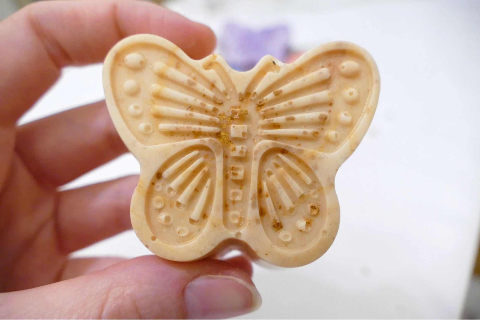 Zlato naravno milo v obliki metulja z vonjem limonske trave, prikazano v dlani za občutek velikosti in nežnosti.