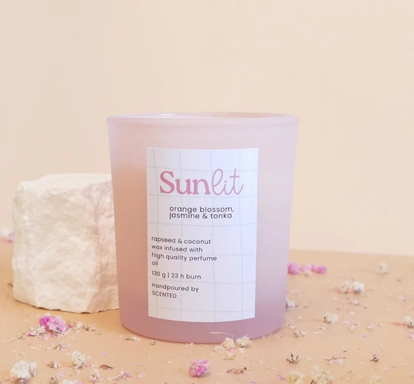 Naravna dišeča sveča Sunlit v steklenem kozarčku bele ali roza barve, z nežno cvetno-orientalsko aromo, ki spominja na poletno jutro.