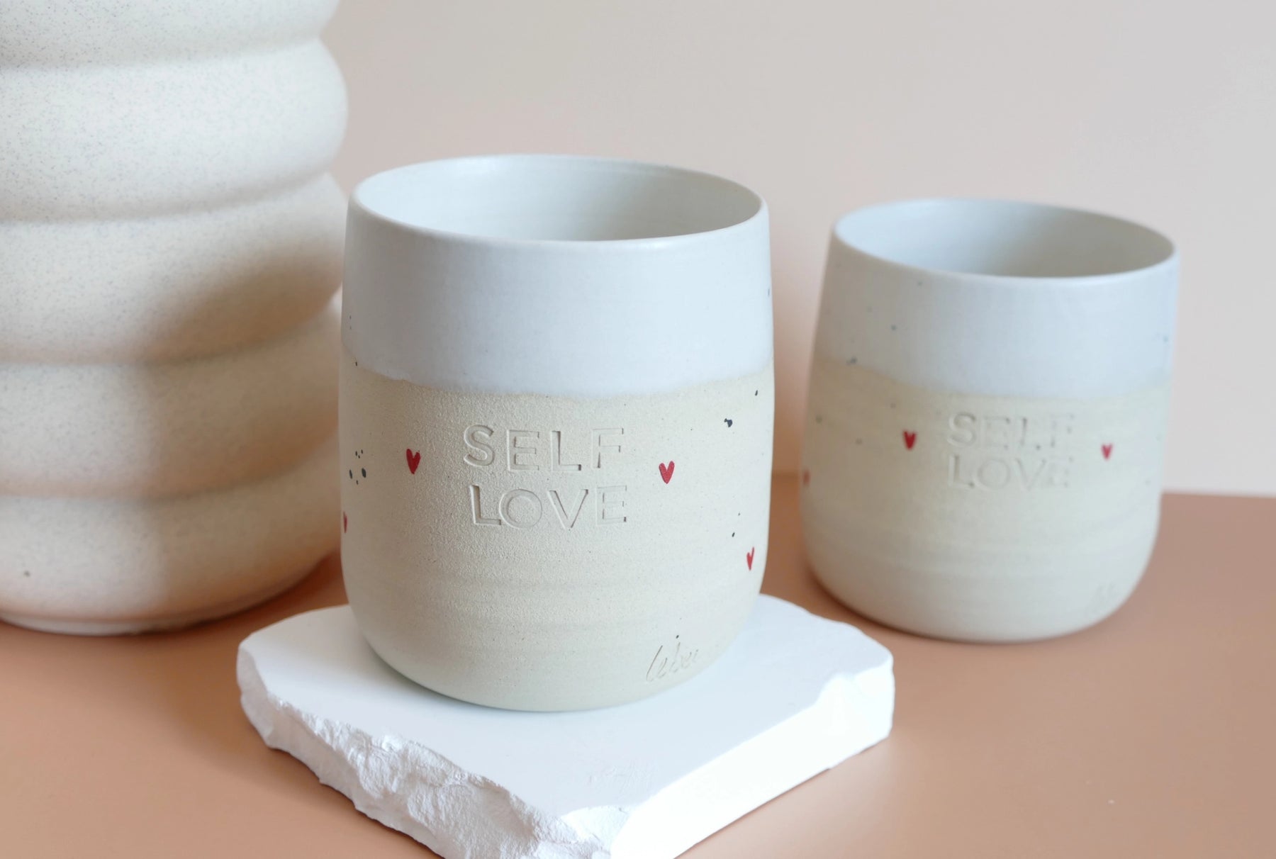 Unikatna dišeča sveča Self-love v ročno izdelani skodelici s sporočilom, obarvana v nežne tone – simbol ljubezni do sebe in trajnostnega razvajanja.