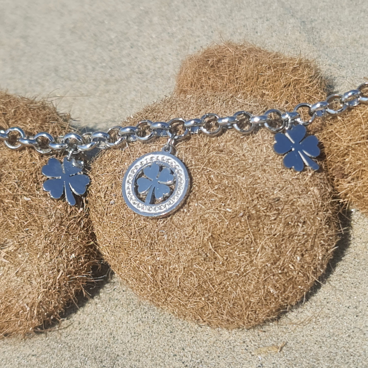 Pulsera de acero con cadena rolo que presenta 2 tréboles de cuatro hojas colgantes y 1 trébol central con piedras blancas