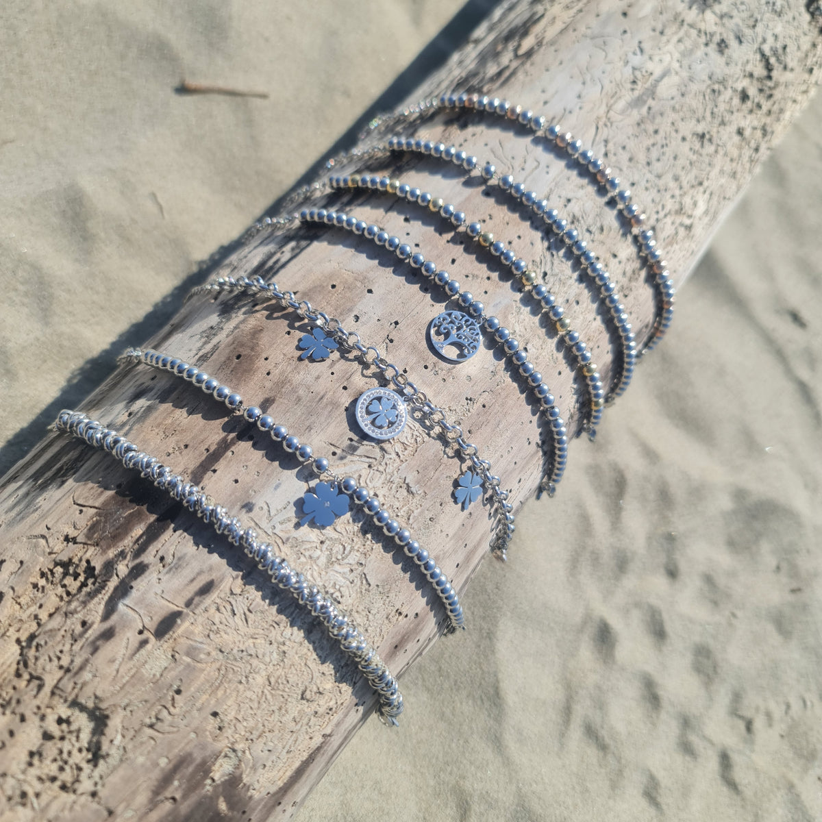 Pulsera de acero con cadena rolo que presenta 2 tréboles de cuatro hojas colgantes y 1 trébol central con piedras blancas