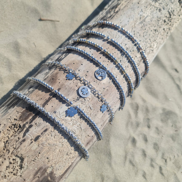 Pulsera de acero con cadena rolo que presenta 2 tréboles de cuatro hojas colgantes y 1 trébol central con piedras blancas