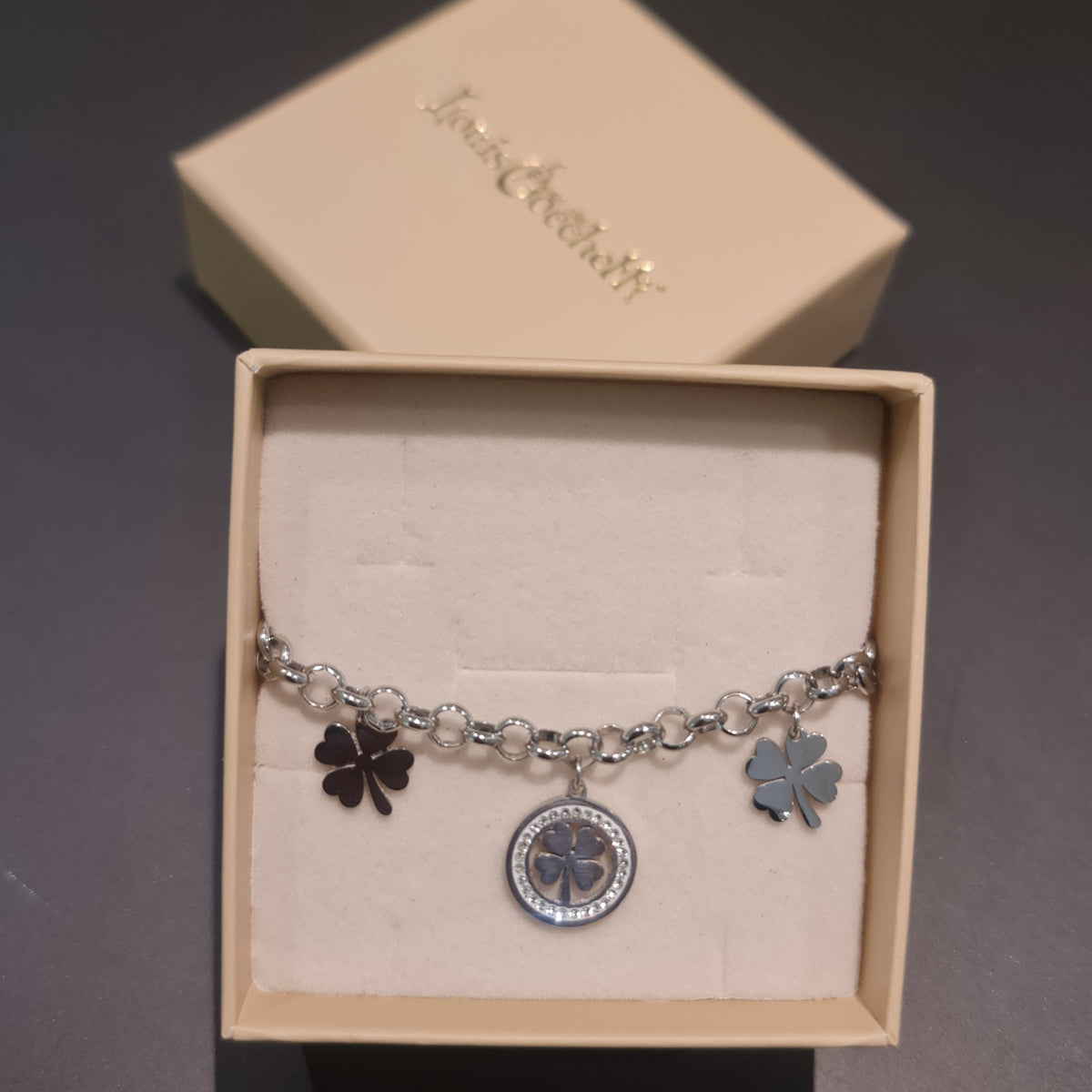 Pulsera de acero con cadena rolo que presenta 2 tréboles de cuatro hojas colgantes y 1 trébol central con piedras blancas