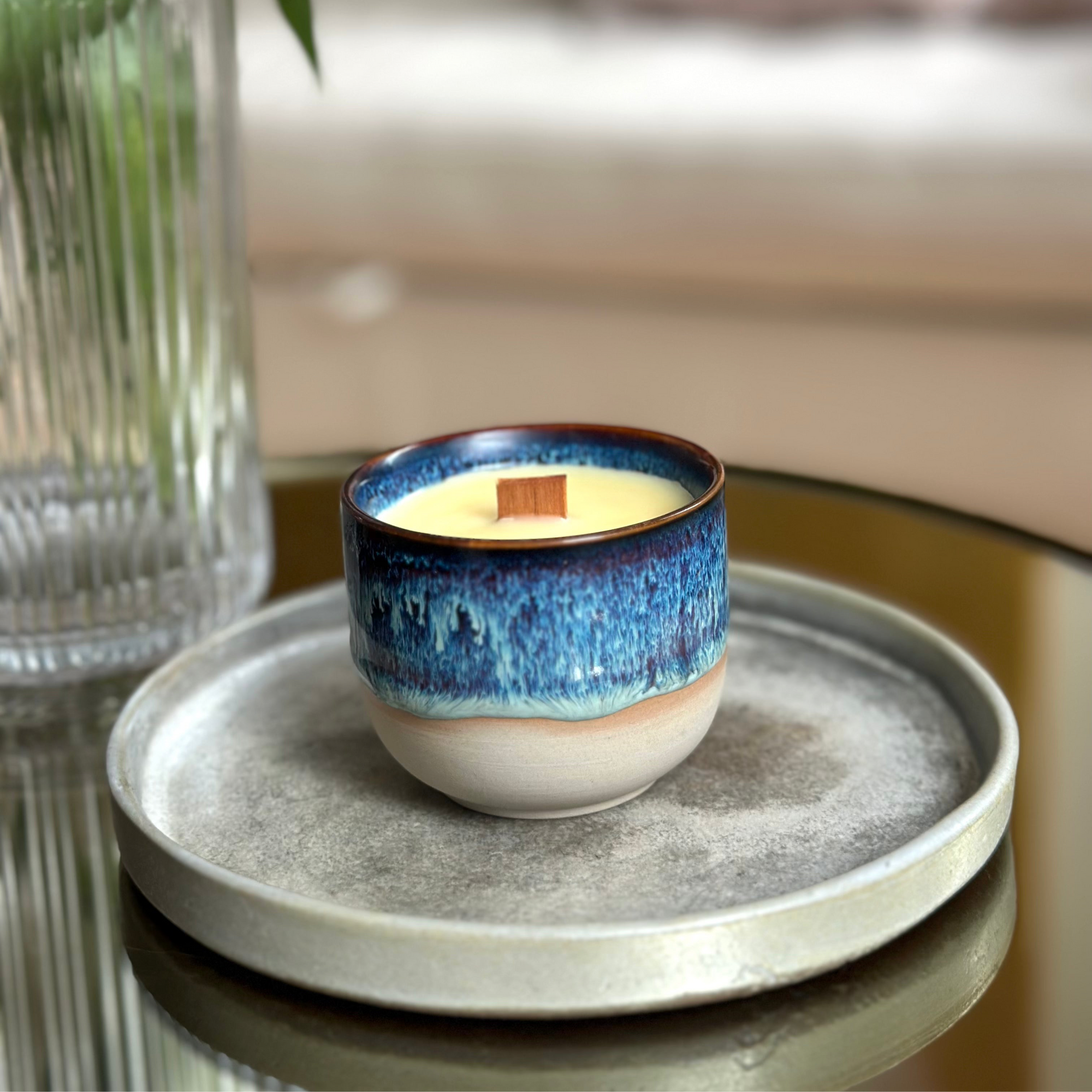 Ceramic candle with blue glaze on a gray plate with a blurred background