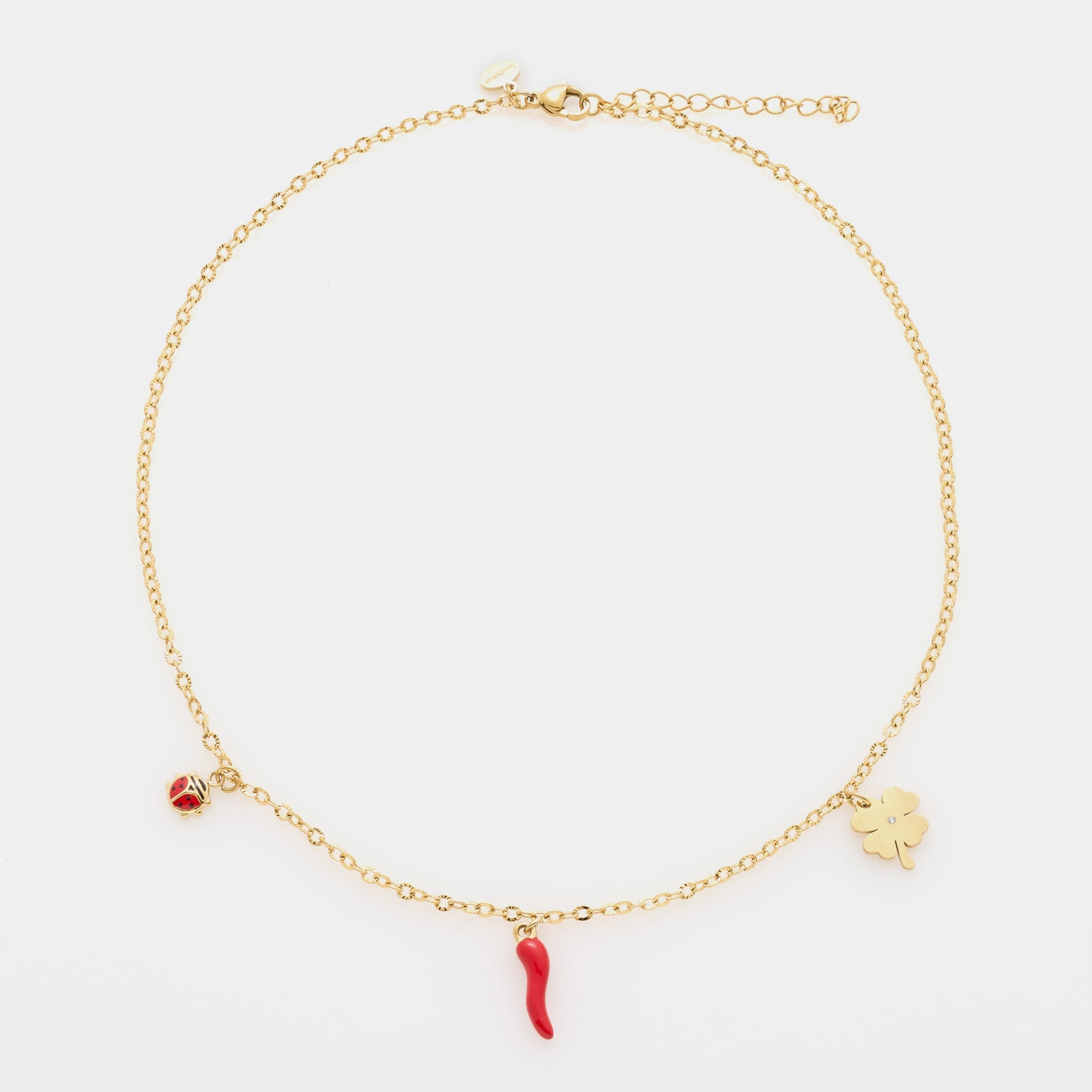 Pulsera de acero chapada en oro con cadena rolò fina y tres charms chapados en oro: trébol, cuerno y mariquita de esmalte rojo