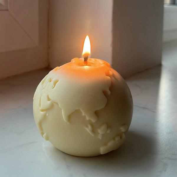 A spherical candle with a design that resembles the Earth's surface, burning with a bright flame.
