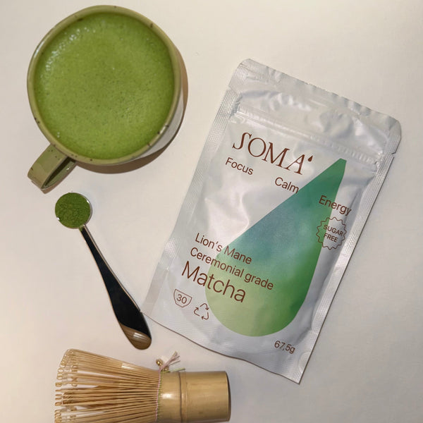 SOMA matcha package with a cup of matcha, spoon, and whisk on a light background