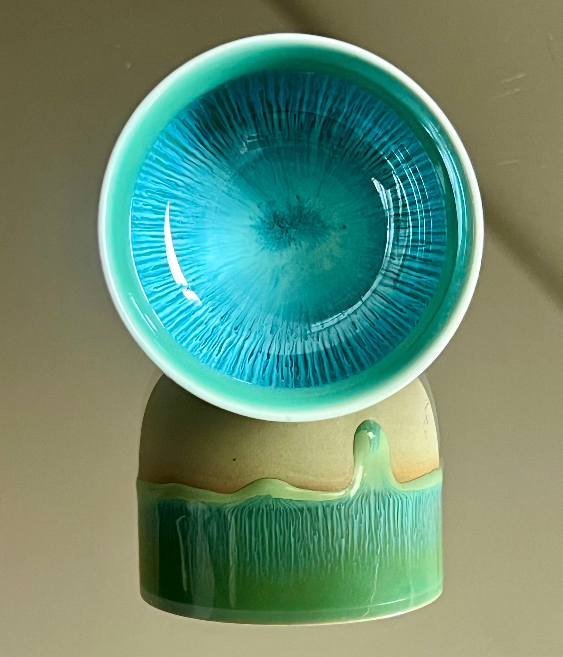Ceramic cup with textured turquoise interior and green exterior on a beige background