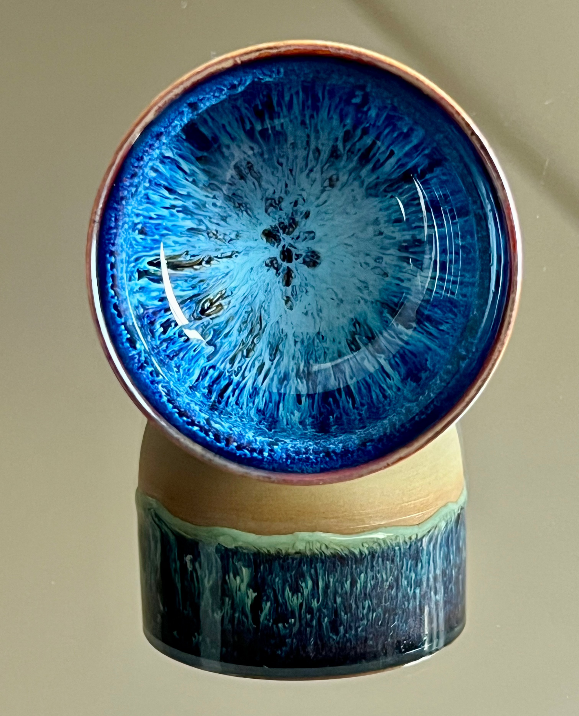 Ceramic cup with blue and green glaze on a beige background