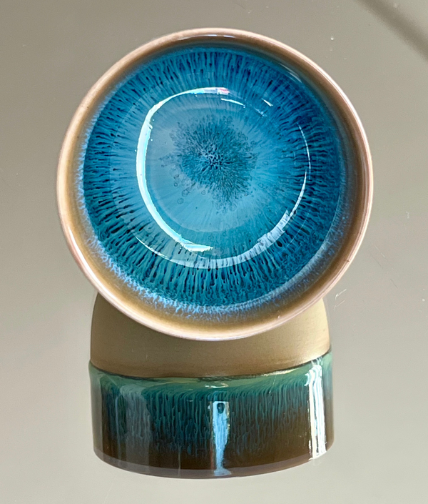 Ceramic cup with blue glaze on a reflective surface