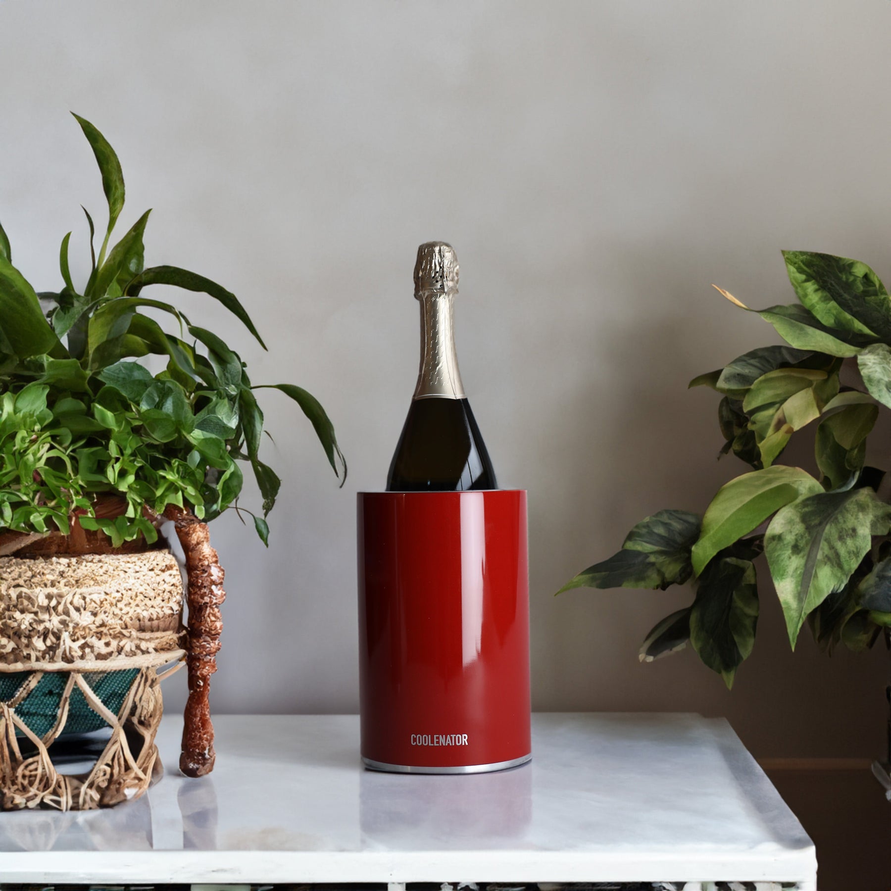 Coolenator Ruby red design wine cooler with a bottle of wine on a white table with plants around