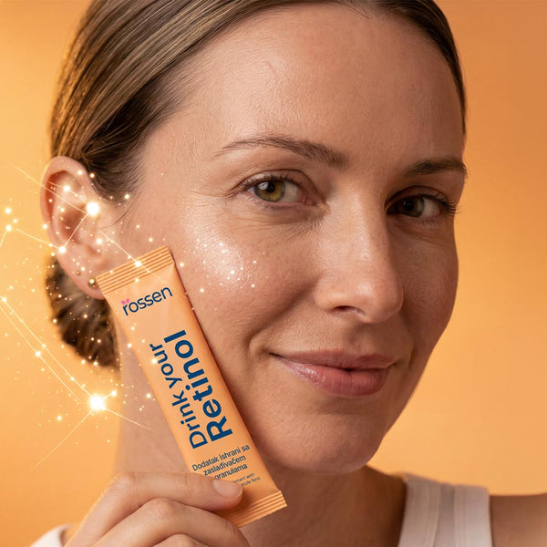 Smiling woman holds an orange sachet labeled 'Drink Your ...' up to her cheek during a product promo shot, warm orange background and sparkles nearby.