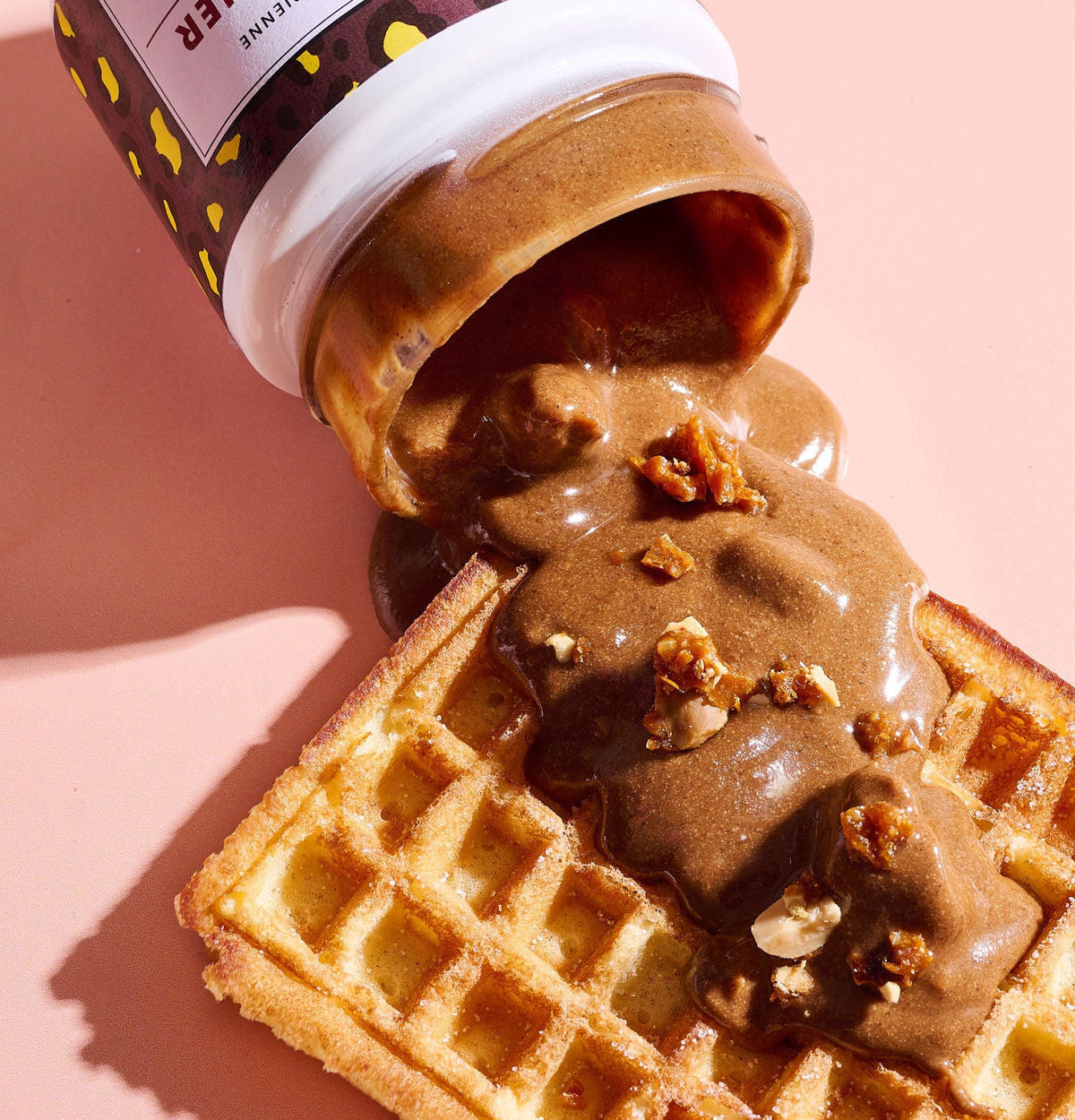 Pot de Pâte à tartiner Chouchou renversé dont la pâte coule sur une gaufre parsemée d'éclats de noix