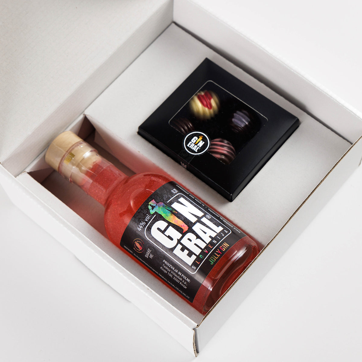 White gift box opened to reveal a bottle of red gin and a small black box of chocolates tucked beside it on the white interior surface, suggesting a gift set.