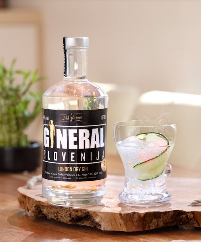 Bottle of Slovenian gin on a wooden board beside a glass with ice and cucumber slice garnish.