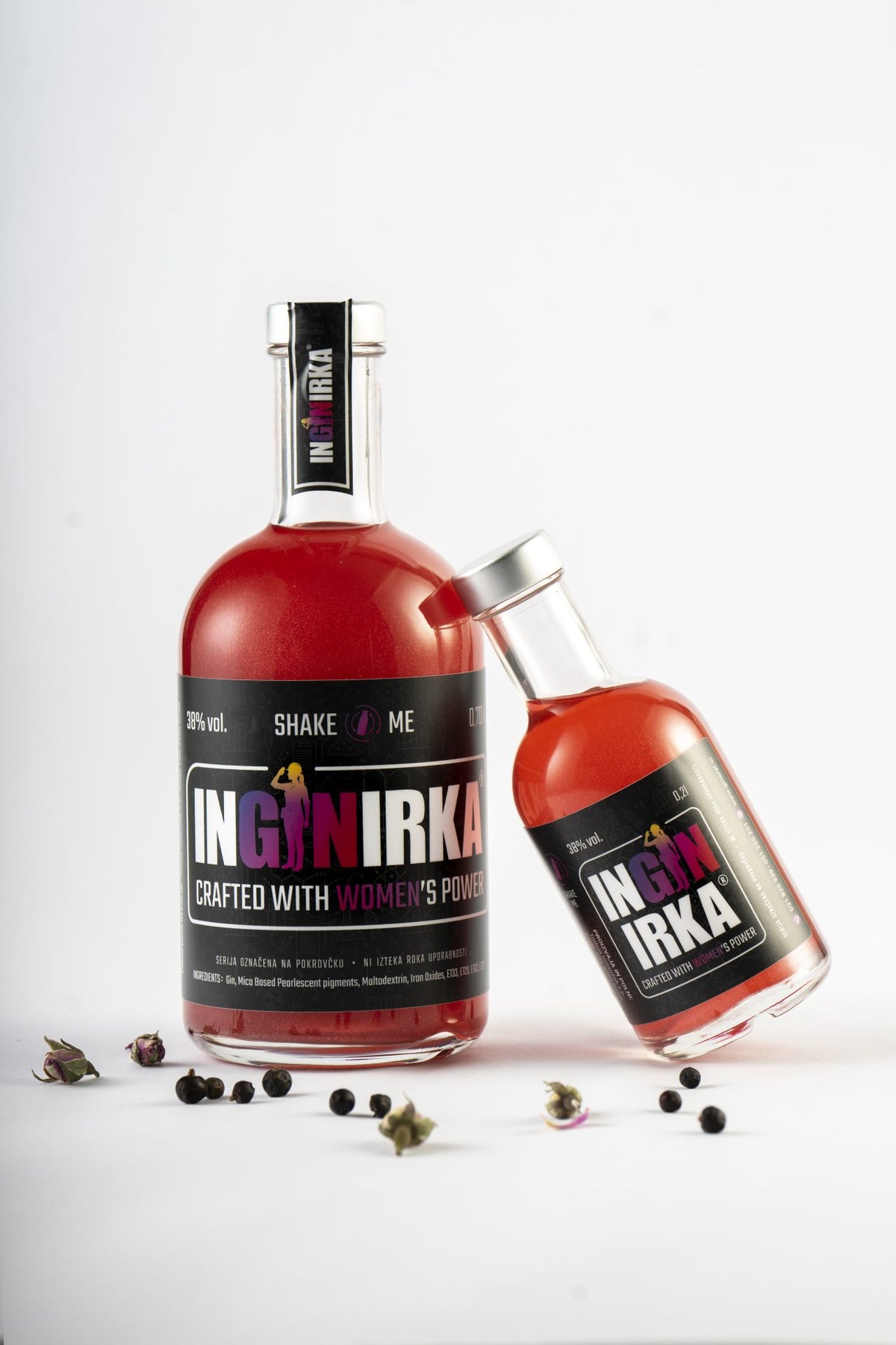 Two red gin bottles on a white background, one upright and the other tilted, with loose botanicals scattered nearby.