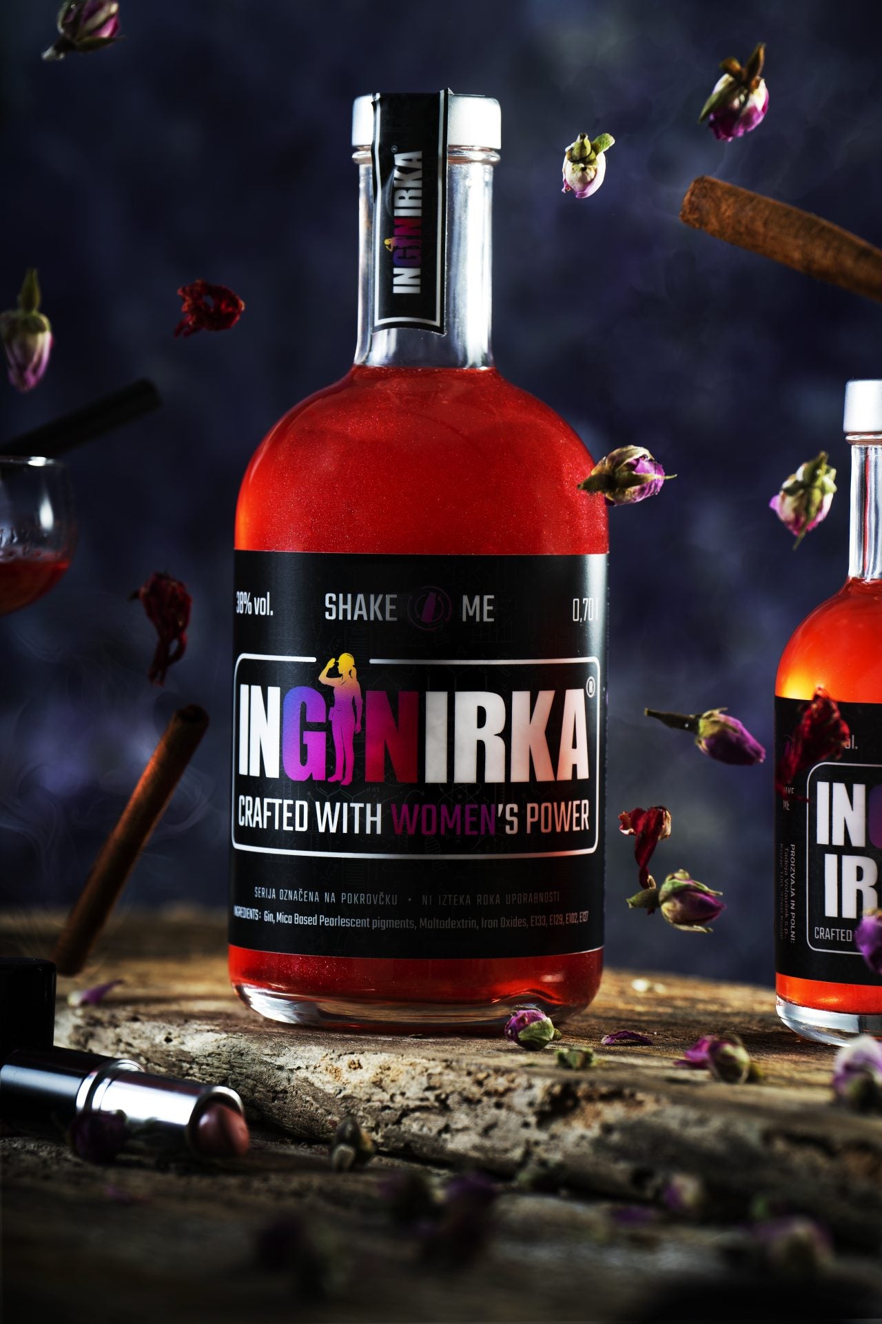 Bottle of INGNIRKA liquor with a bold black label, red liquid, surrounded by floating rosebuds and cinnamon sticks in a dark scene.