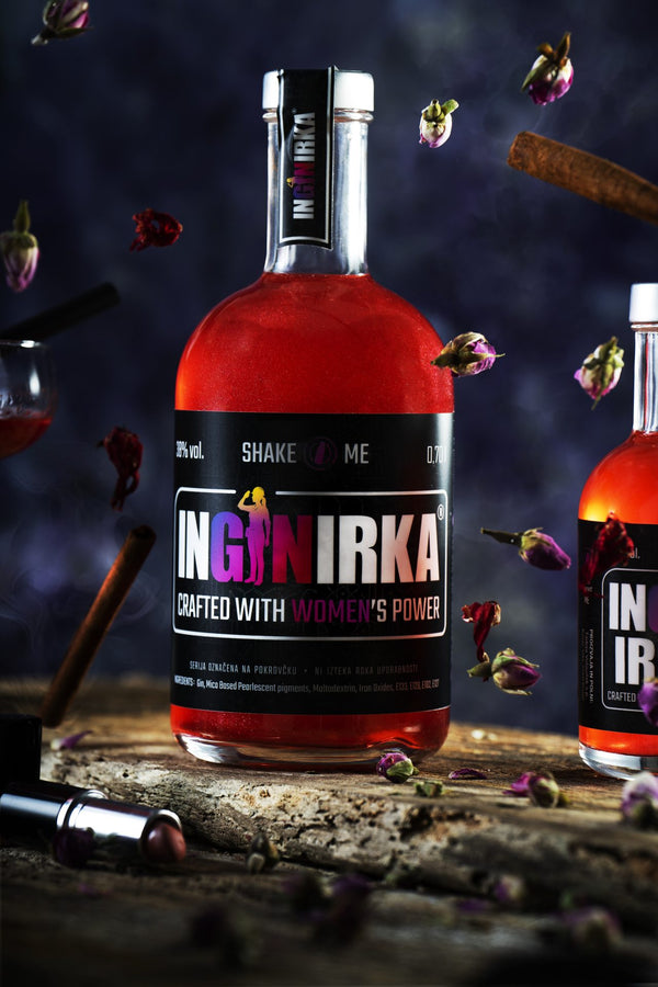 Bottle of INGNIRKA liquor with a bold black label, red liquid, surrounded by floating rosebuds and cinnamon sticks in a dark scene.