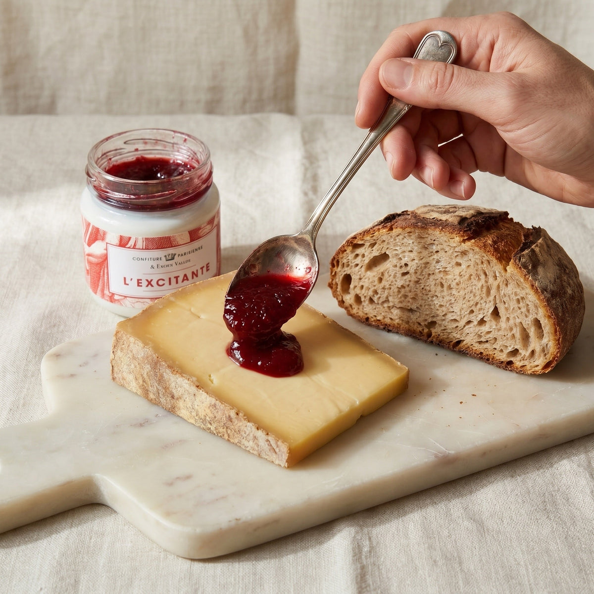 Confiture L'Excitante x Fabien Vallos déposée à la cuillère sur une tranche de fromage, pain de campagne à côté
