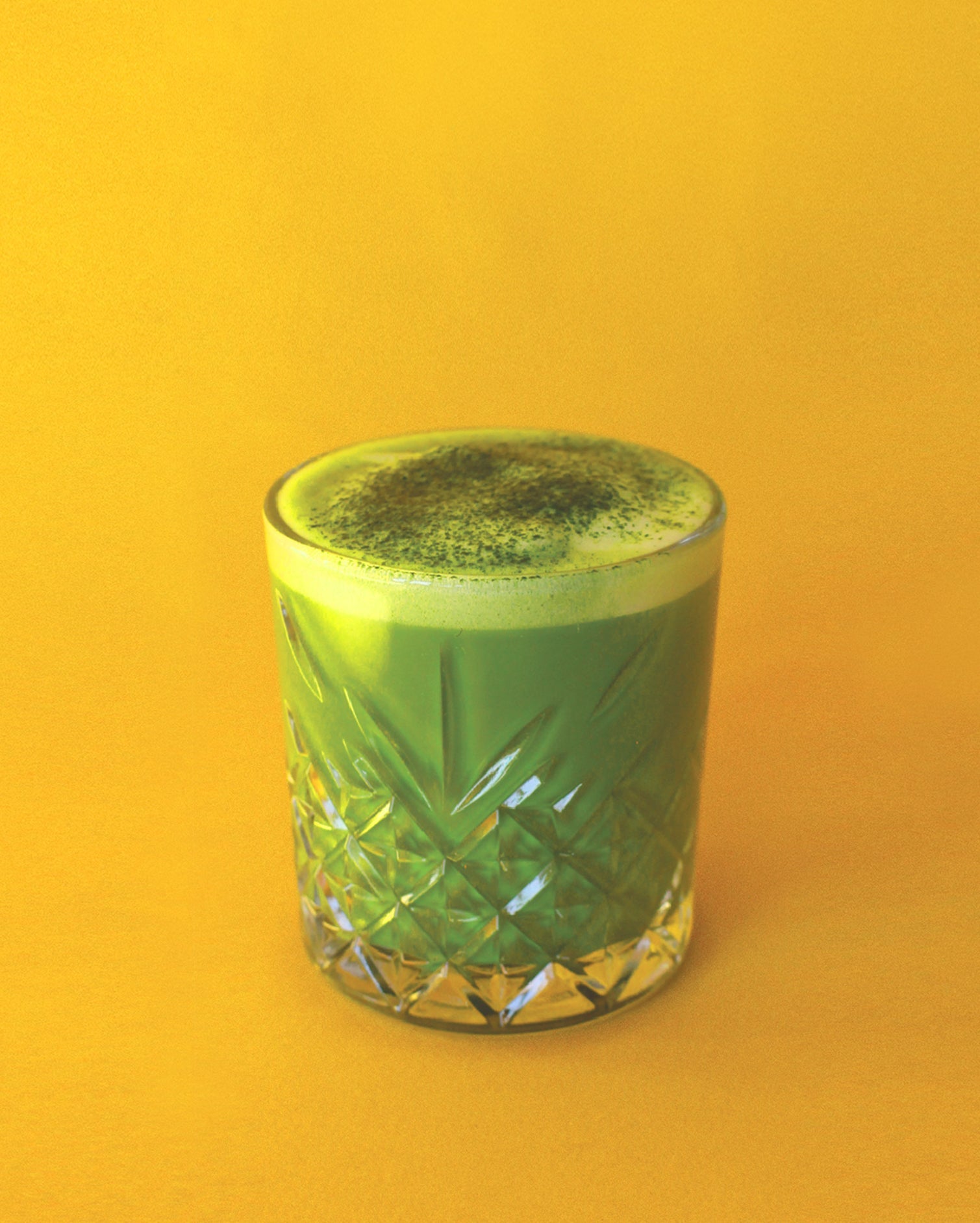 Matcha 7A whisked in a carved glass on a yellow background