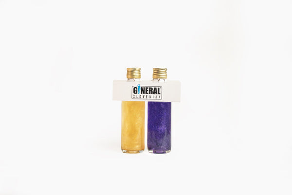 Two small glass bottles filled with yellow and purple glitter, held by a white plastic holder labeled 'GENERAL SLOVENIJA'