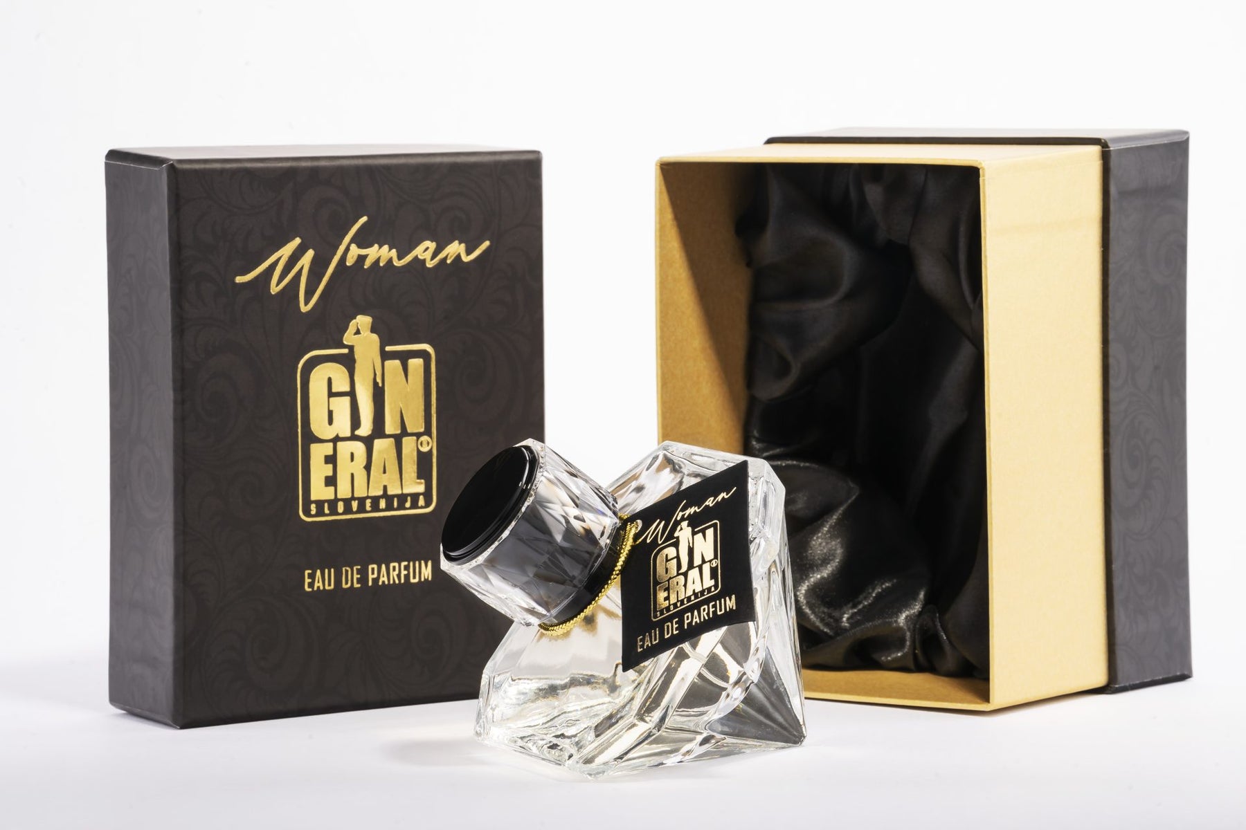 Clear glass perfume bottle with black label and gold text placed in a black-and-gold box set; satin lining visible inside the open box.