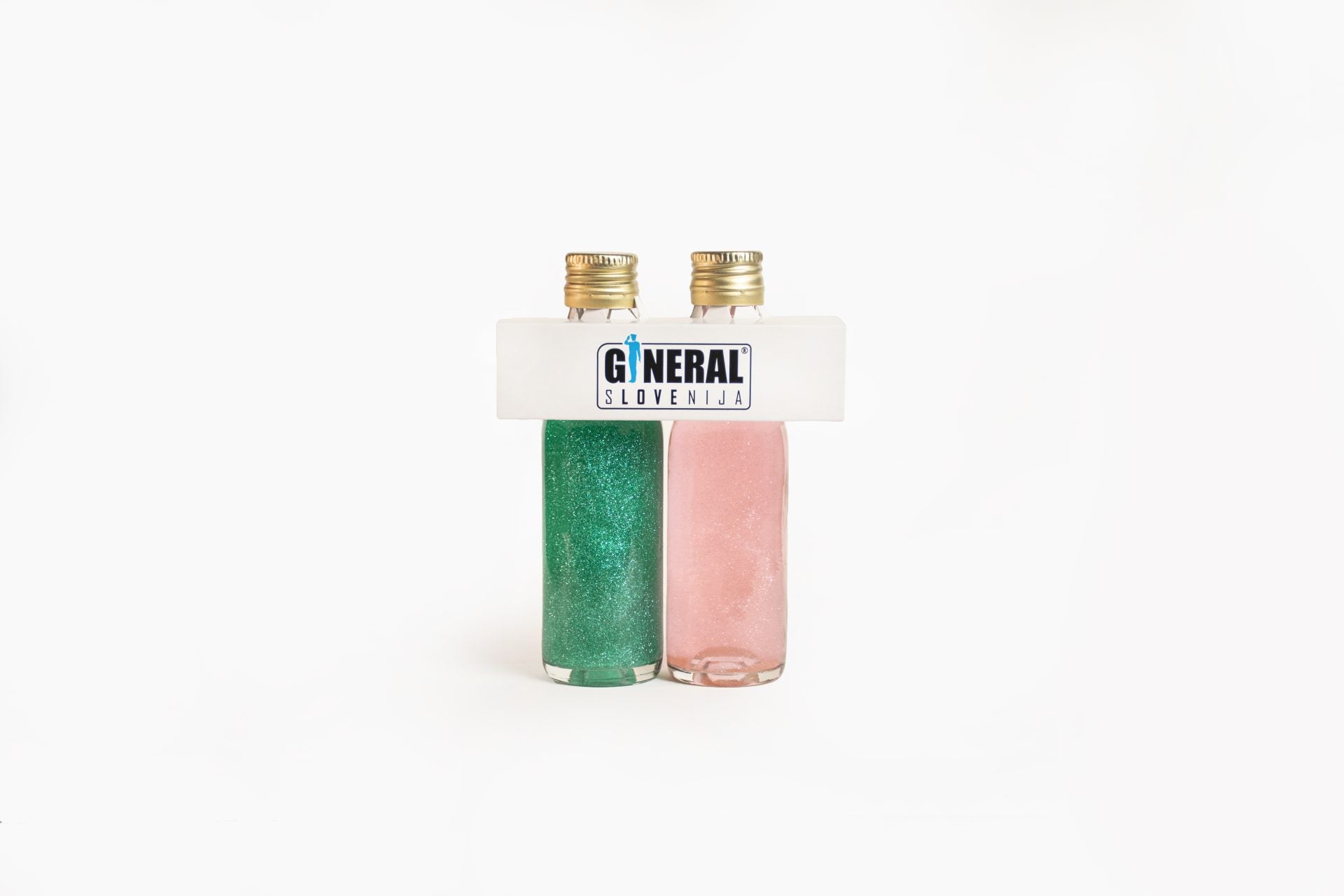 Two glitter nail polish bottles, green and pink, standing side by side with a white carrier labeled 'GENERAL SLOVENIJA' on top.
