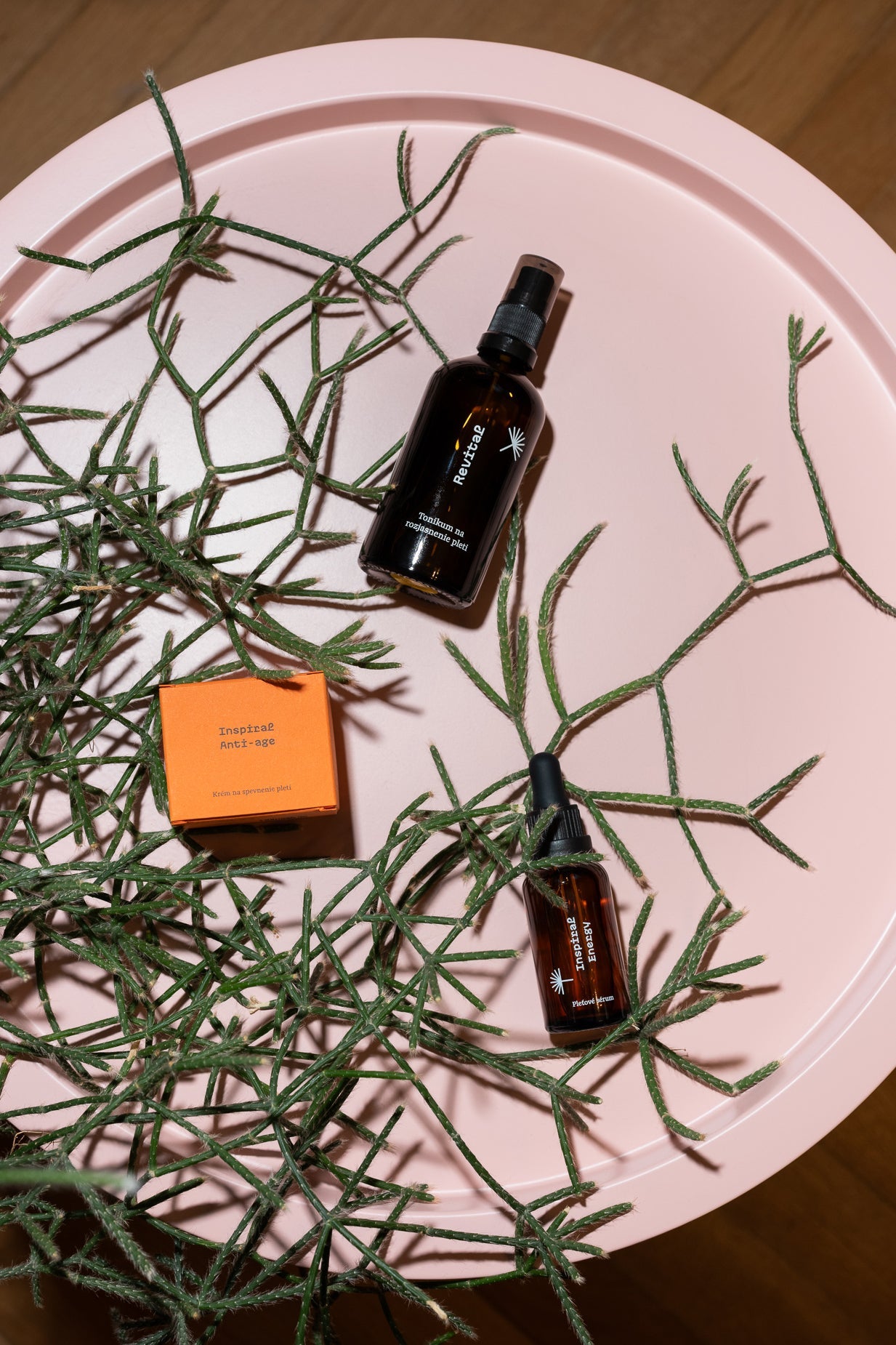 Anti-age sada Spevnenie a omladenie pleti Modrá púpava – tonikum Revital, sérum Inspiral Energy a krém Inspiral Anti-age naaranžované na ružovom podnose s prírodnými vetvičkami