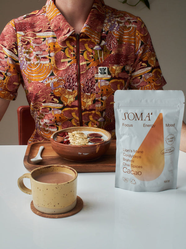 Soma Cacao Focus pouch with a speckled mug of cacao and a breakfast bowl with figs and banana