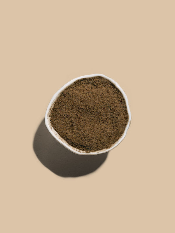 Bowl of roasted hojicha powder on a beige background