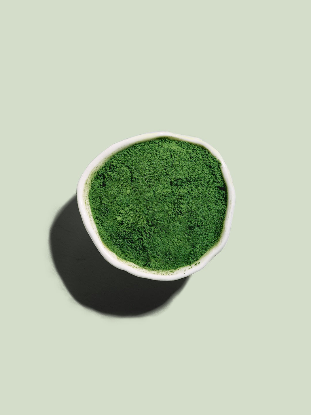 Bowl of bright green Matcha 7A powder on a sage green background