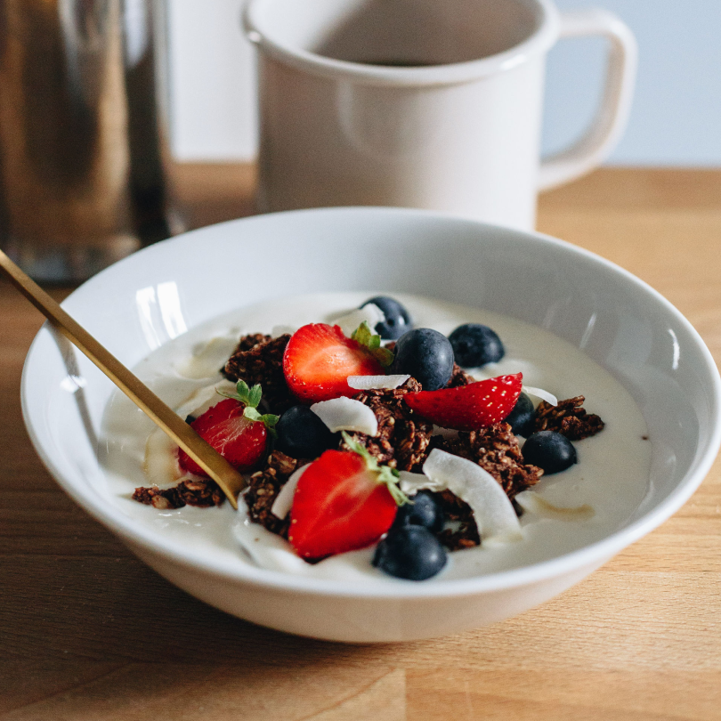 Bol de granola bio au chocolat avec yaourt, fruits rouges et copeaux de coco pour le petit-déjeuner